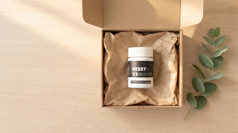 Caja de Reset abierta con el frasco Reset V3 adentro, sobre una mesa de madera